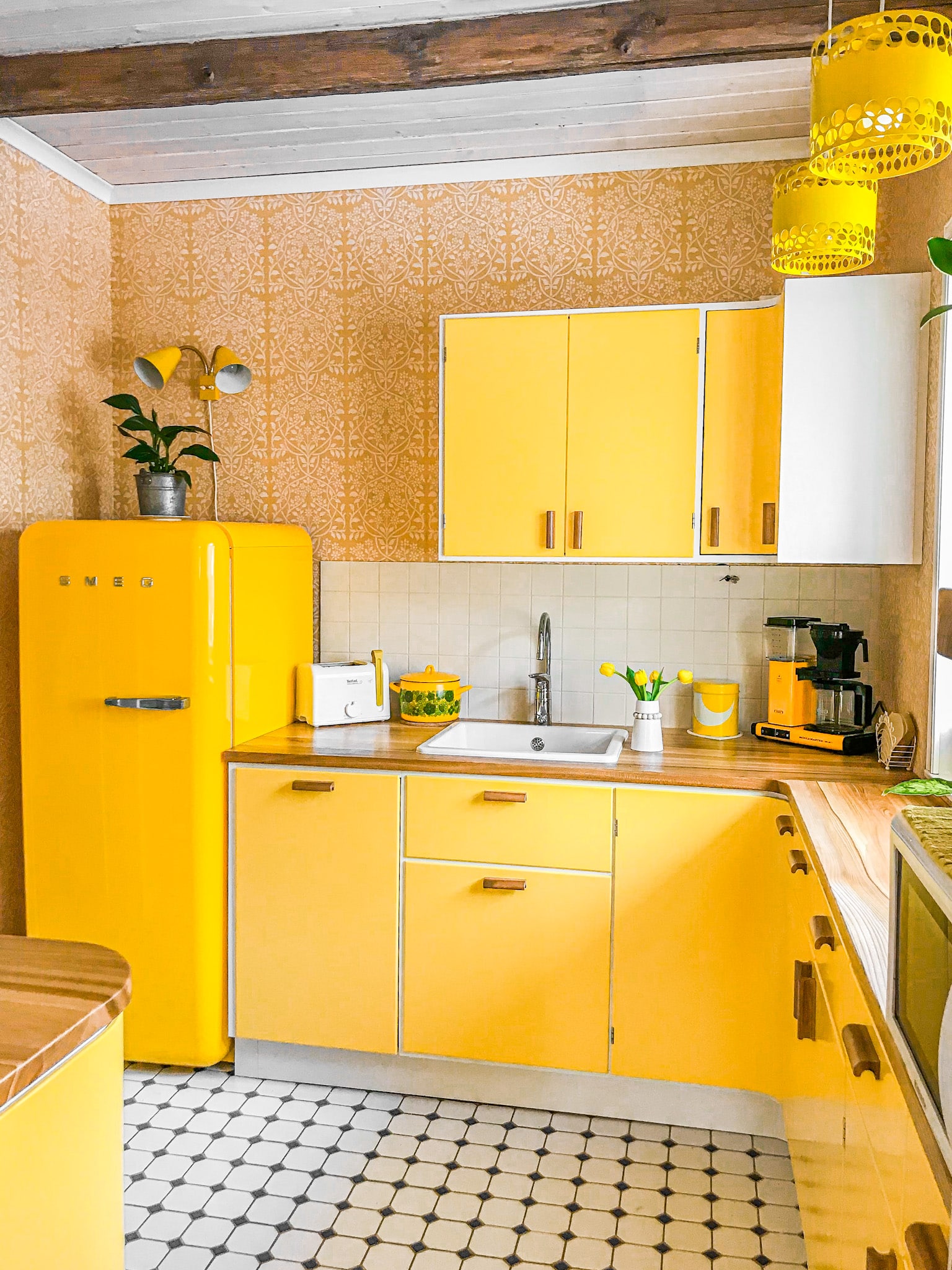 V&auml;rik&auml;s 50-luvun keitti&ouml; keltaisilla kaapistoilla ja retroj&auml;&auml;kaapilla &ndash; T&auml;m&auml; kodikas keitti&ouml; huokuu 1950-luvun tunnelmaa kirkkaankeltaisten kaapistojen, puisten vetimien ja ikonisen SMEG-retroj&auml;&auml;kaapin ansiosta. Valkoiset neli&ouml;laatat mustilla yksityiskohdilla luovat ajattoman lattian, kun taas kuviollinen tapetti ja puiset kattopalkit tuovat l&auml;mp&ouml;&auml; tilaan. Rottinkivarjostimilla varustetut riippuvalaisimet ja pirte&auml;t yksityiskohdat, kuten kahvinkeitin ja astiat, t&auml;ydent&auml;v&auml;t nostalgisen mutta toimivan kokonaisuuden.